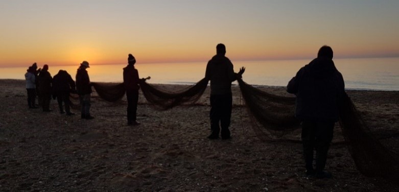 A group of people carrying a net off the beach at sunset, by Tony Kelly.