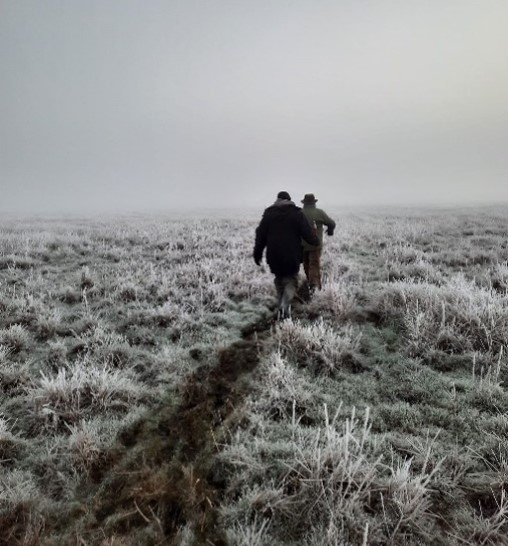 Two people walking across a frozen marsh in the fog, by Jade Gunnell.