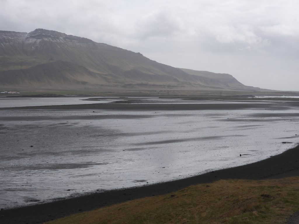 A mudflat in front of distant hills. The day is grey and misty looking giving the image a murky look. Photo by Carole Davis.