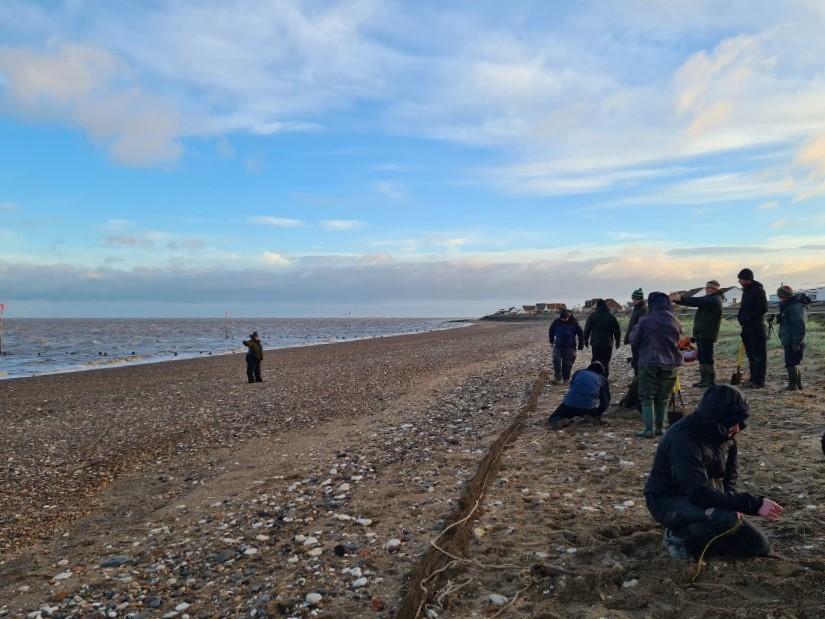 Photograph of the team setting cannon nets on a shingle beach against a blue sky with white clouds. Photo by Kirsty Turner.