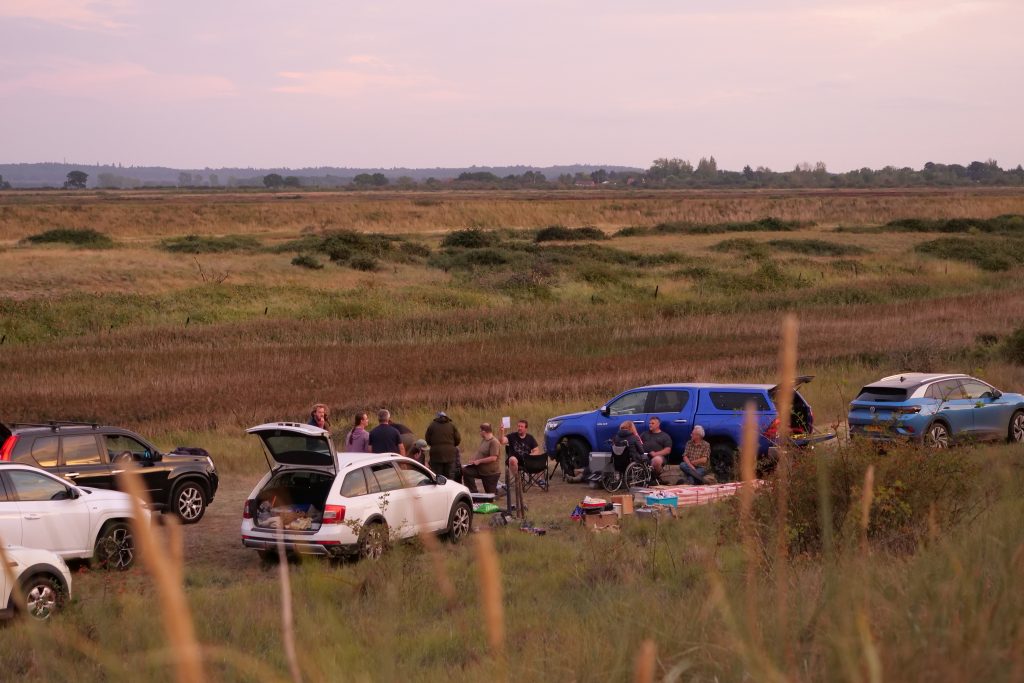 A group of people surrounded by cars in a field.